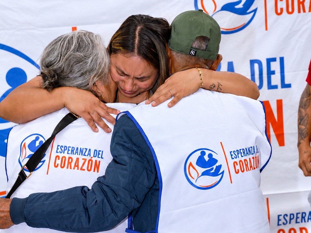 Una joven abraza a dos adultos mayores que llevan el chaleco del programa durante un reencuentro